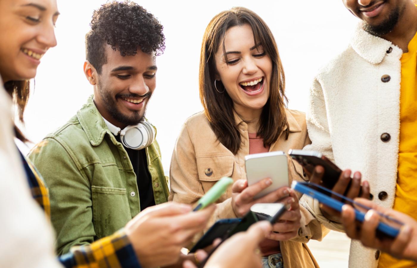 A group of people are gathered close looking at their smart phones together.