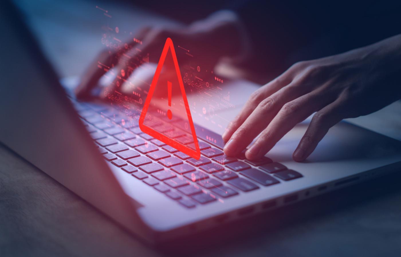 A red warning triangle hangs over a laptop. A website has been hacked.