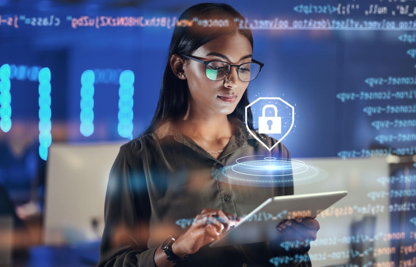 A women looks at a tablet and an image of a lock hovers above representing cybersecurity.