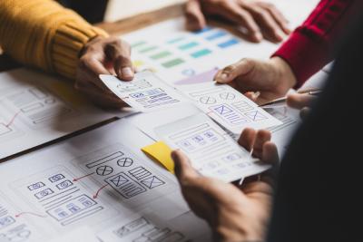 A group of designers collaborates on website navigation sketches, reviewing wireframes and layout elements on paper.