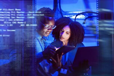 Two professionals look at a tablet together with code overlaying the image.