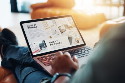 A laptop with a website on the screen sits on a mans legs.
